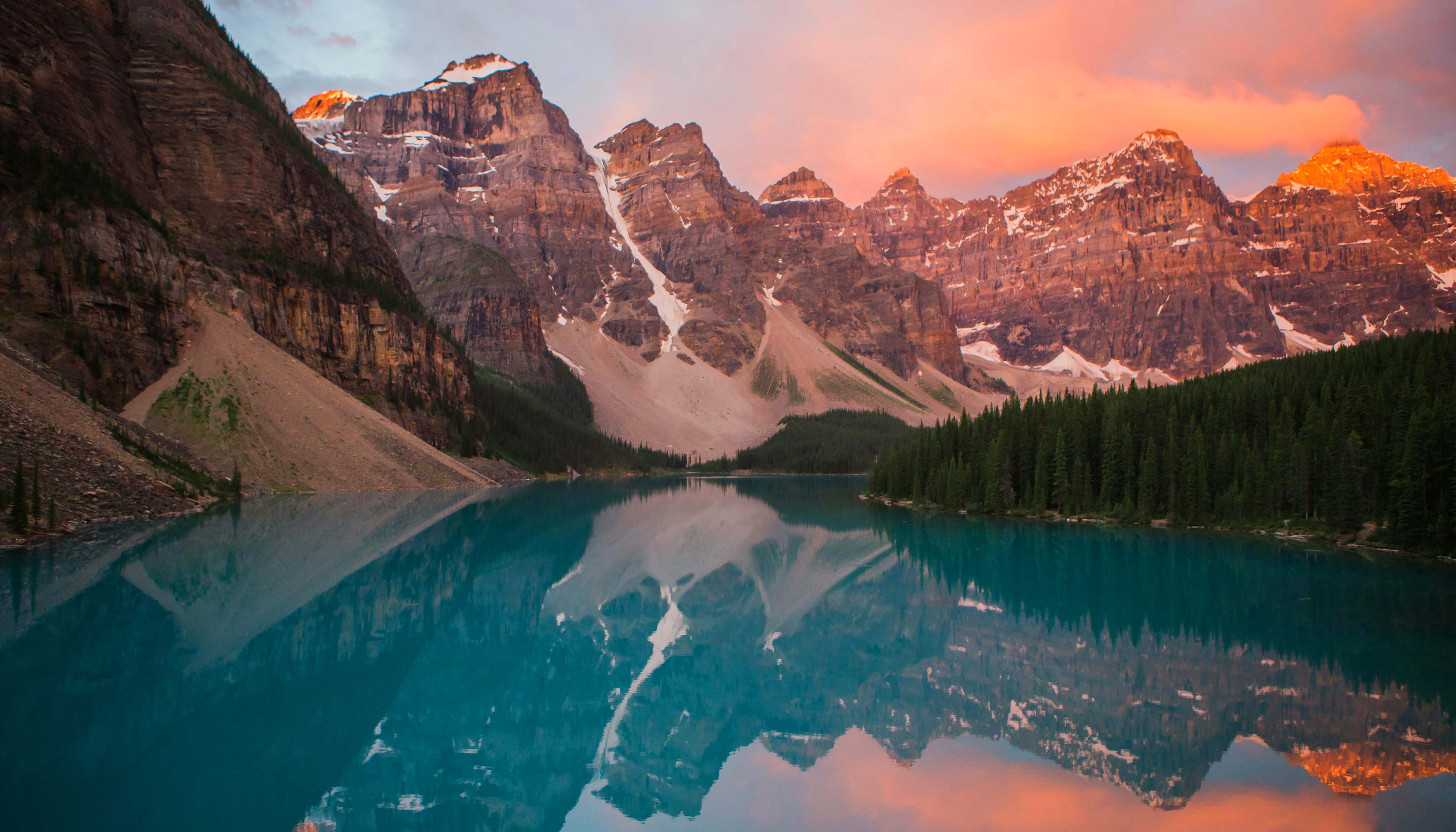 A Lake At Sunset Surrounded By Trees And Mountains